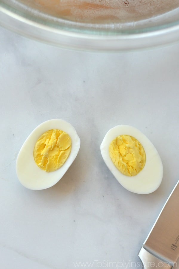 closeup of a hard boiled egg cut in half with yolk showing with a knife laying beside it.