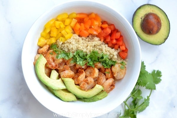 closeup of a bowl of Shrimp, quinoa, sliced avocado and red, yellow, orange peppers