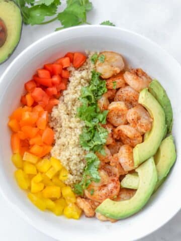 closeup of a bowl of Shrimp, quinoa, sliced avocado and red, yellow, orange peppers
