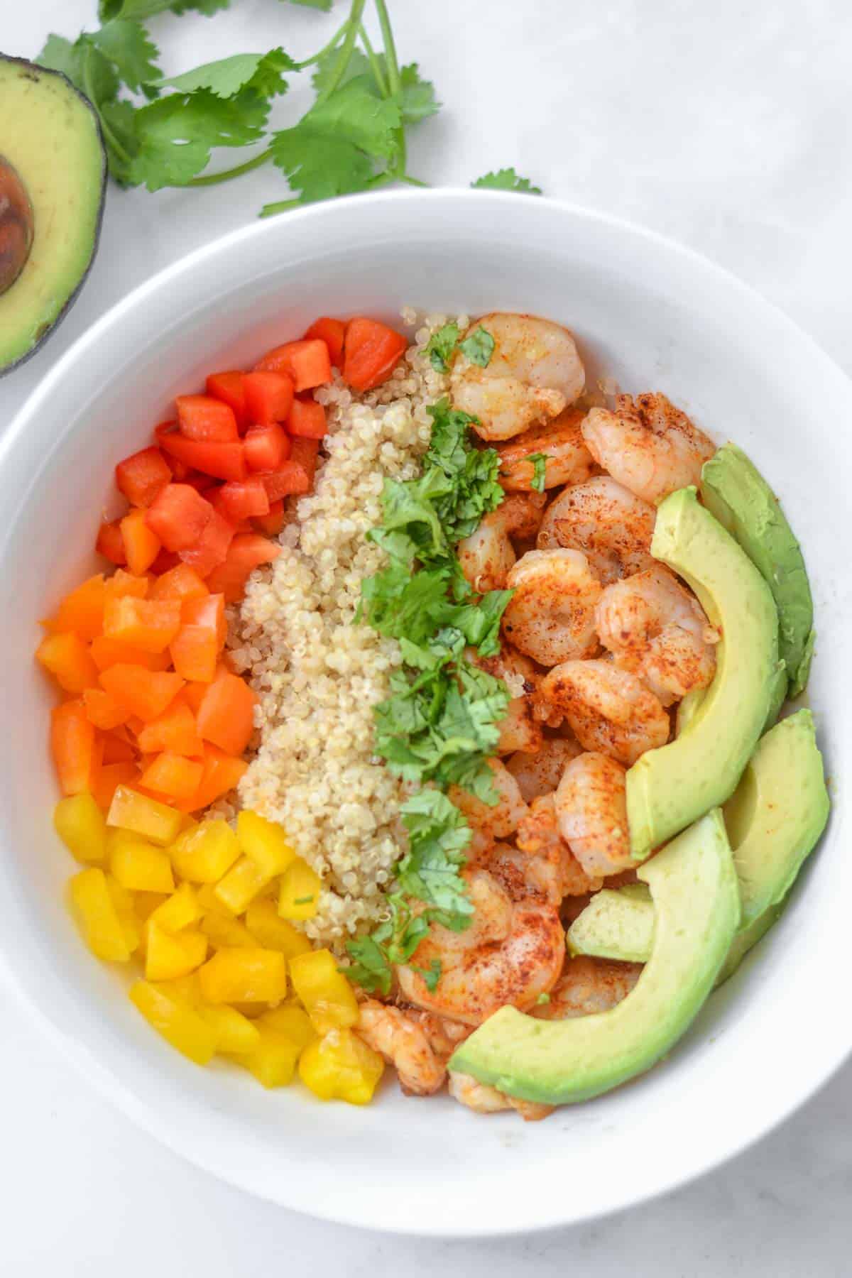 closeup of a bowl of Shrimp, quinoa, sliced avocado and red, yellow, orange peppers