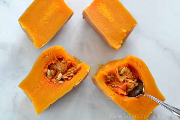 cut butternut squash halves on a countertop with a spoon scooping seeds and pulp