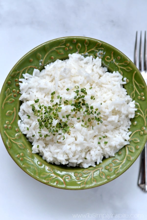 This easy Coconut Rice is so amazing with it's rich flavor! Turn plain jasmine rice into a wonderful, aromatic side dish that's perfect for Asian inspired curry dishes, stir-fries, and more! Coconut Rice in a green bowl topped with chives.