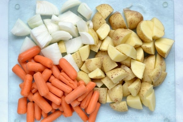 diced potatoes, carrots and onions on a glass cutting board