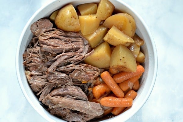 A white bowl full of pot roast, cut potatoes and baby carrots
