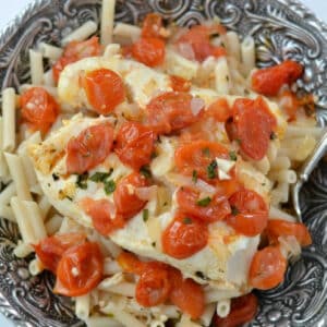 closeup of Italian cod topped with tomatoes and basil over penne pasta.