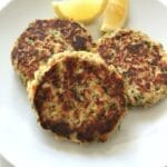 three tuna patties on a white plate with lemon wedges