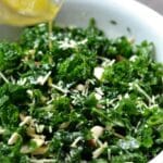 closeup of kale salad with parmesan cheese and sliced almonds with lemon vinaigrette being poured over.