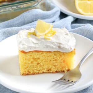 slice of lemon poke cake with white icing on a white plate.