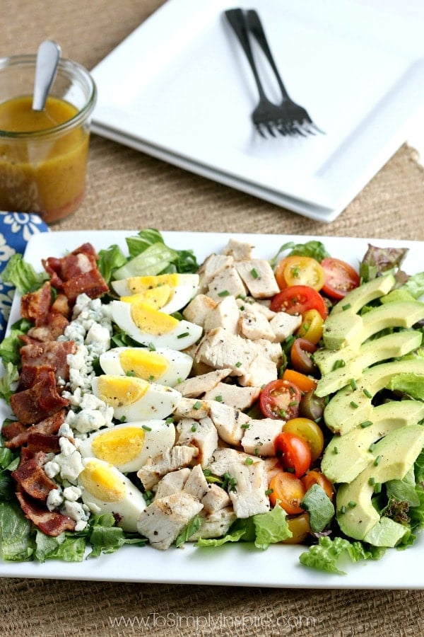 Cobb Salad on a rectangle white plate with bacon, chicken, hard boiled eggs, tomatoes, avocado and blue cheese