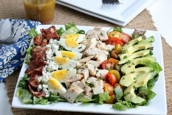 A plate of food on a table with Salad, chicken, bacon, tomatoes, hardboiled eggs and avocado