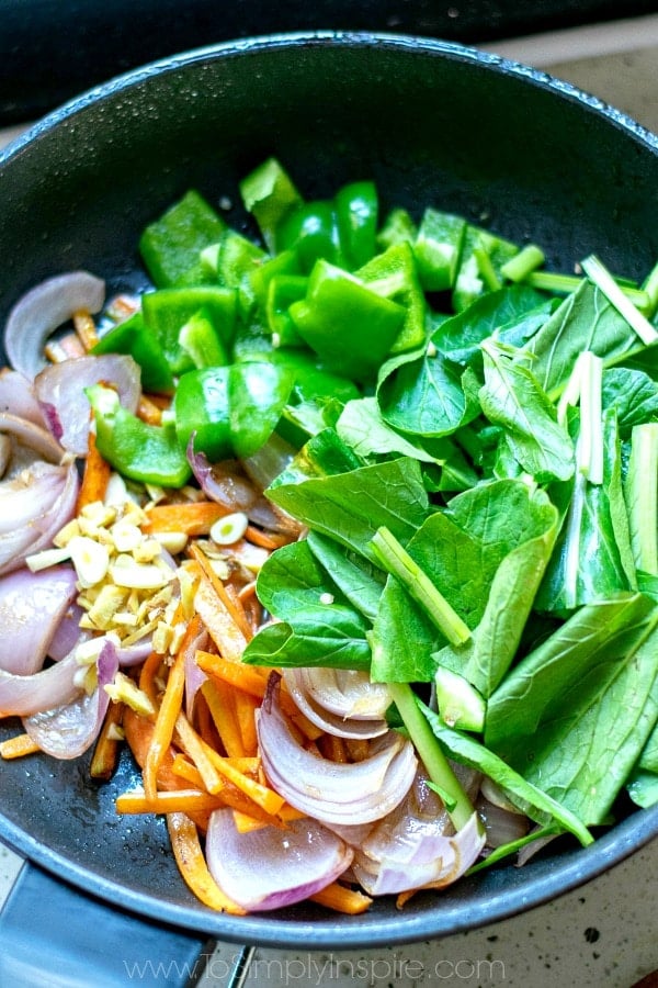 spinach green peppers red onions and carrots cooking in a pan