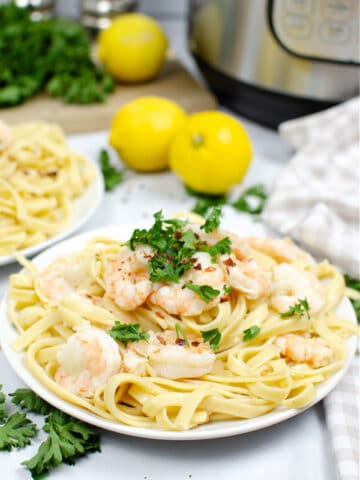 shrimp scampi over fettuccine noodles on a white plate with 2 lemons