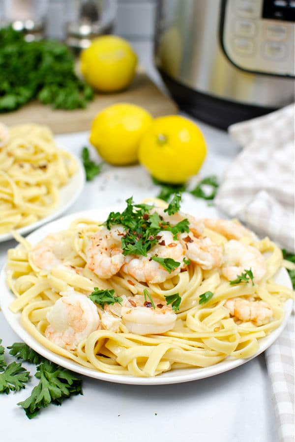 shrimp scampi over fettuccine noodles on a white plate with 2 lemons