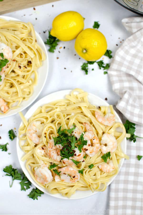 two white plates full of shrimp scampi over fettuccini noodles