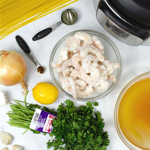 uncooked shrimp in a bowl surrounded by fresh parsley, lemons, chicken broth and fettuccini noodles