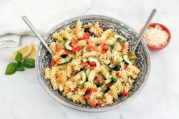 Italian pasta salad in a big silver serving bowl with 2 serving spoons