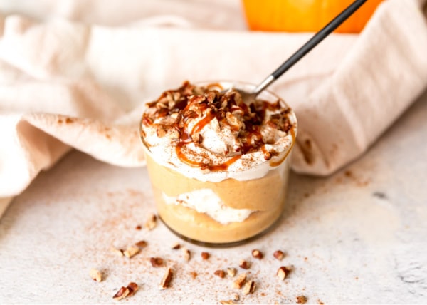 pumpkin cheesecake trifle in a wide mouth glass with a spoon