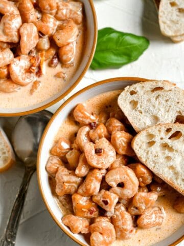 closeup of sweet potato gnocchi with shrimp in a white bowl with 2 slices of bread