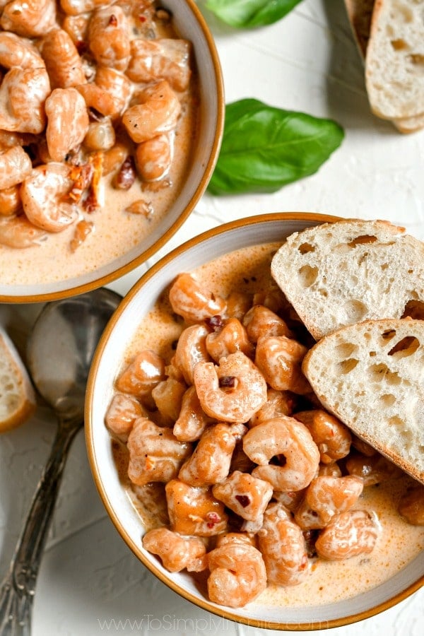 closeup of sweet potato gnocchi with shrimp in a white bowl with 2 slices of bread 
