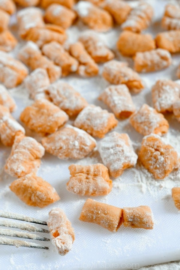 uncooked sweet potato gnocchi on a white cutting board covered in flour
