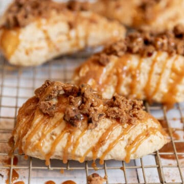 four scones drizzled with caramel sauce on a metal cooling rack