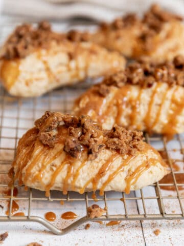 four scones drizzled with caramel sauce on a metal cooling rack