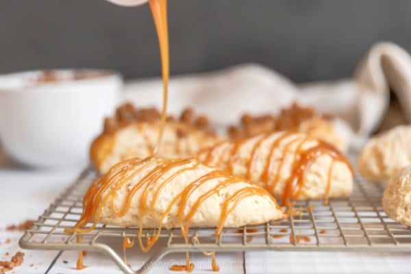 apple scones on a cooking rack being drizzled with caramel sauce