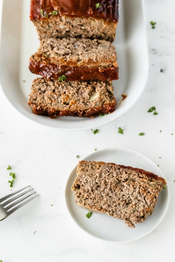 slice of meatloaf on a white plate with meatloaf on a platter in the background