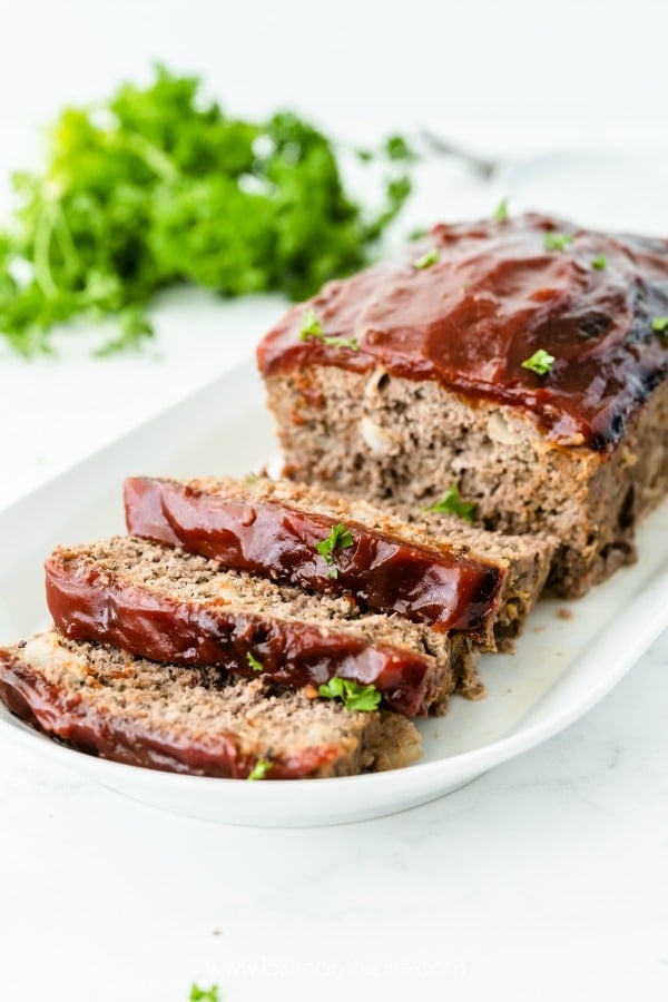 Meatloaf with 3 slices cut on a white plate with parsley in the background