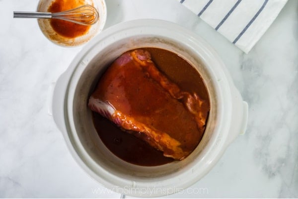 uncooked pork shoulder in a slow cooker with barbecue sauce