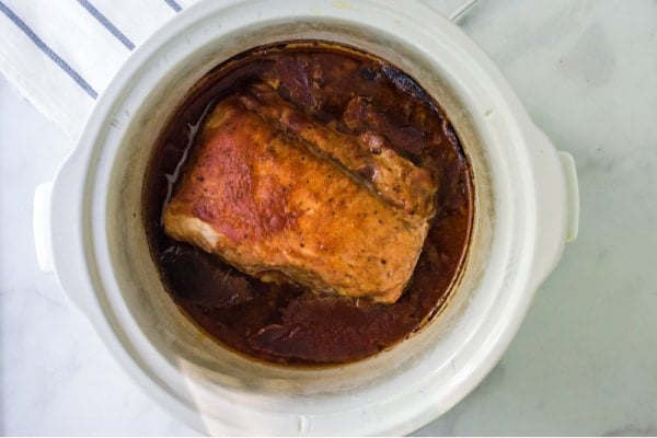 pork shoulder roast covered in bbq sauce in a white slow cooker