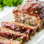 meatloaf recipe topped with tomato glaze on a white plate with 3 slices cut