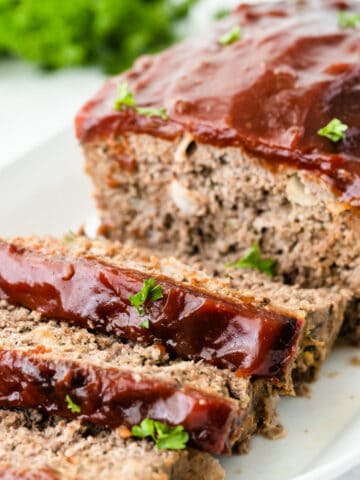 meatloaf recipe topped with tomato glaze on a white plate with 3 slices cut