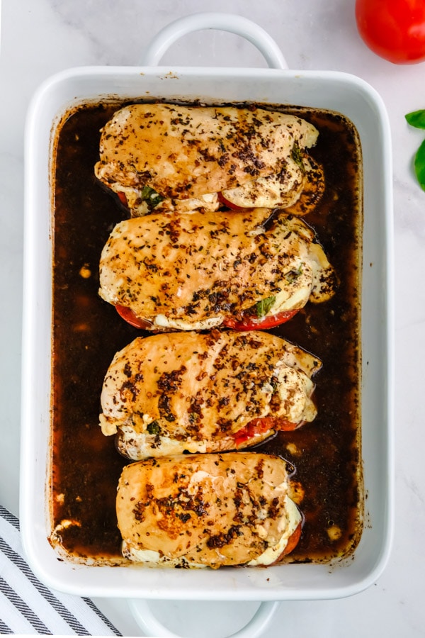 Four chicken breasts drizzled with balsamic vinegar in a white casserole dish