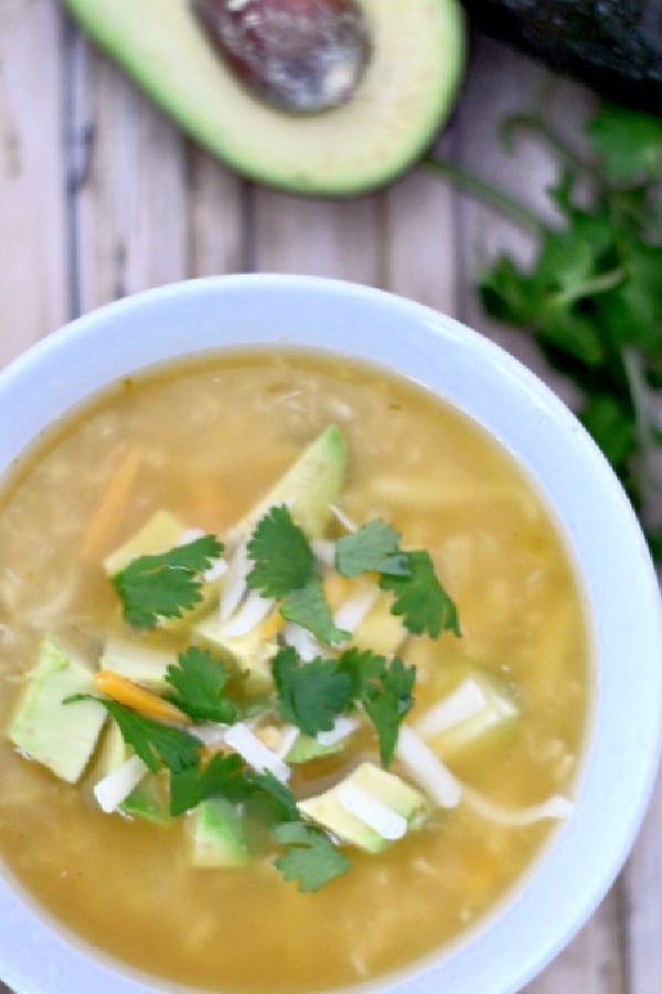 a white bowl full of white chicken chili on a wood table with half an avocado