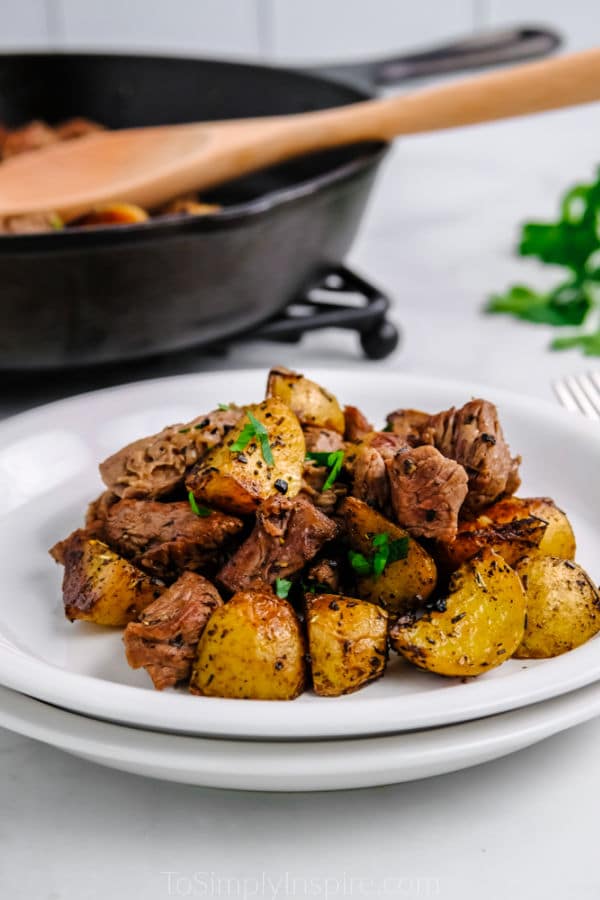 butter steak bites and potoes on a white plate with cast iron skillet in the background