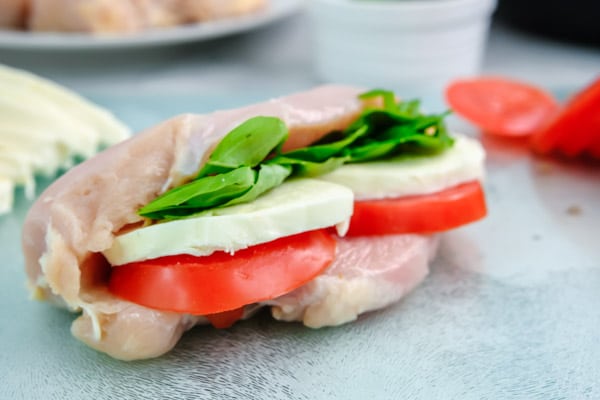 closeup of raw chicken breast stuffed with tomato slice, mozzarella and fresh basil leaves