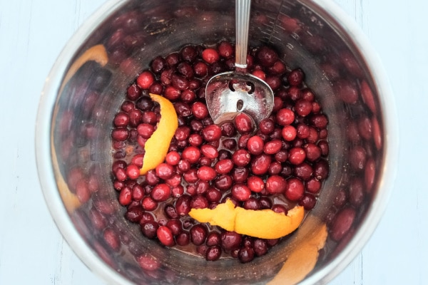 uncooked cranberries and orange slices in an instant pot with a spoon