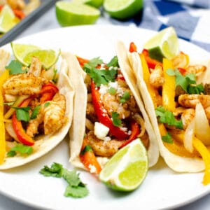 three shrimp fajits with red and orange bell peppers on a white plate