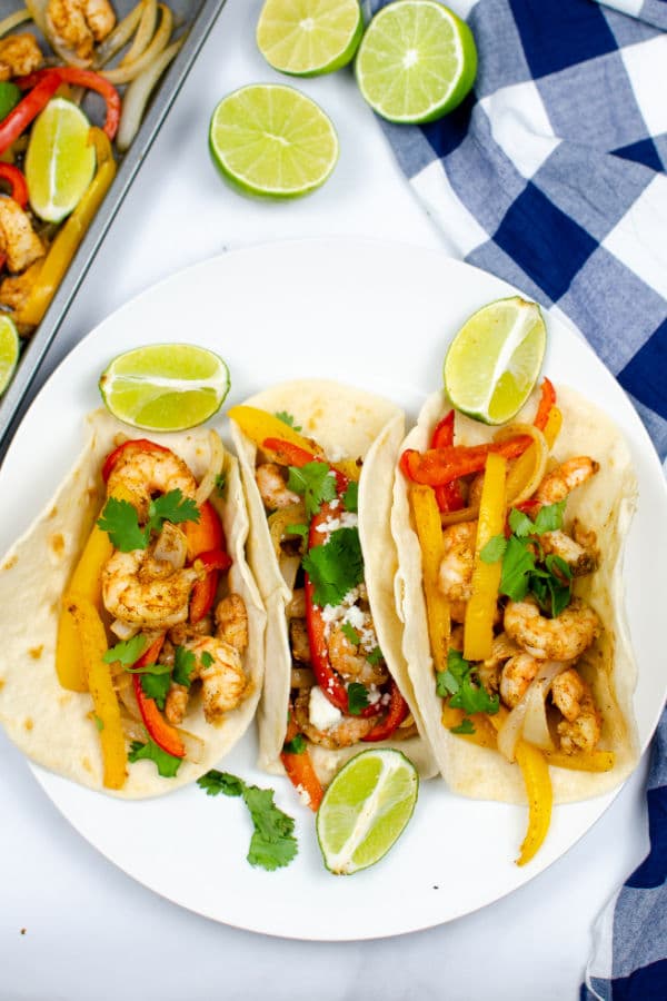 three shrimp fajitas on a white plate with lime slices
