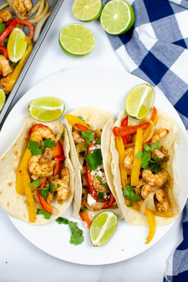 three shrimp fajitas on a white plate with lime slices 