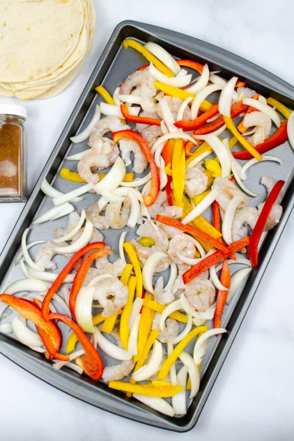 uncooked shrimp, sliced onions sliced red and yellow peppers on a baking sheet