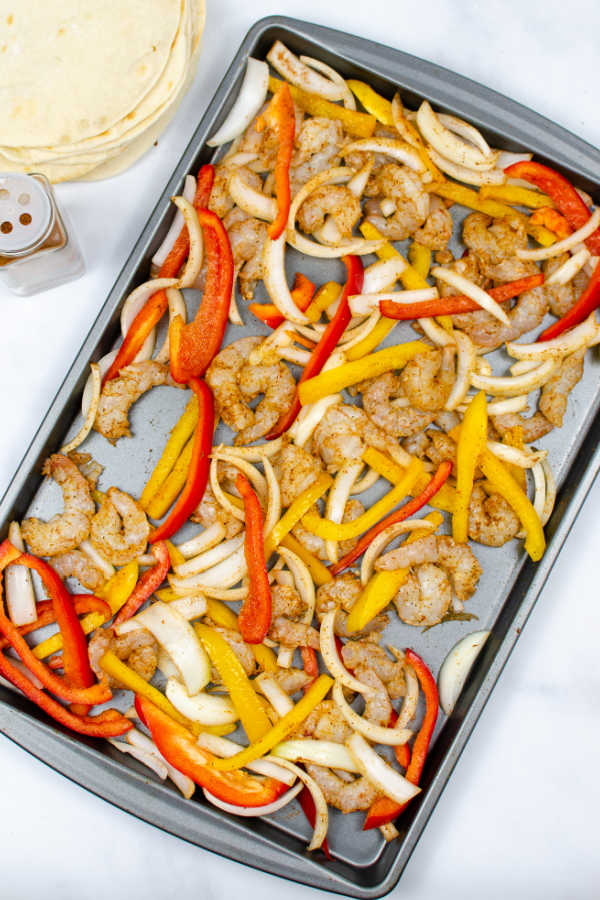 shrimp, sliced onions sliced red and yellow peppers on a baking sheet