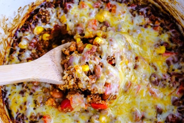 cheesy mexican casserole being served out of a crock pot with a wooden spoon