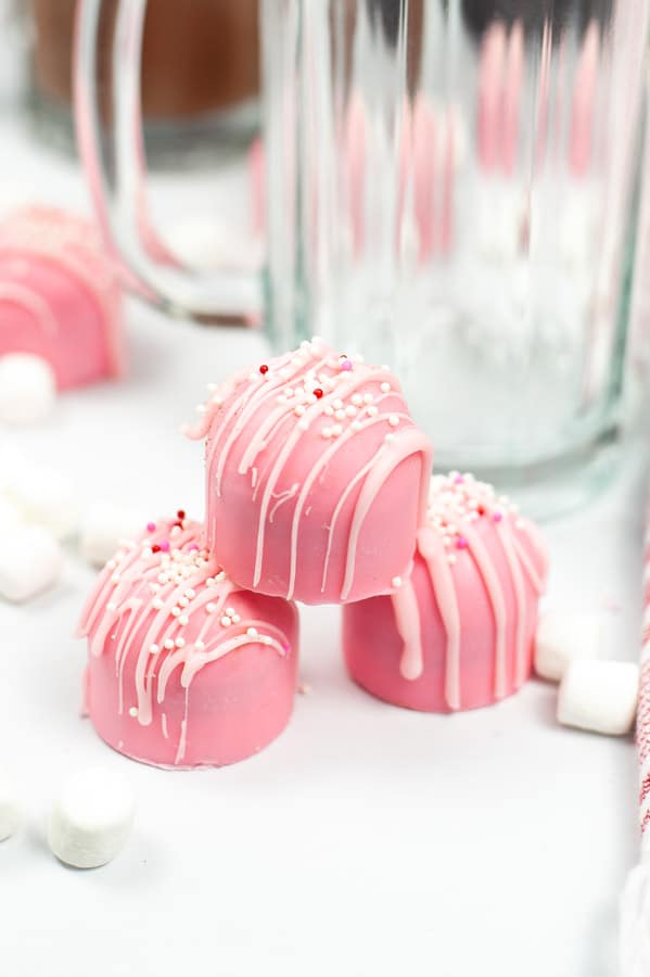 three pink hot chocolate bombs stacked in front of a glass mug