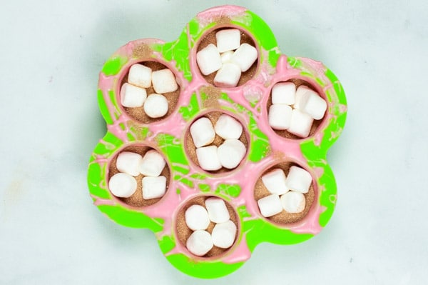 seven circle silicon molds filled with hot cocoa powder and marshmallows