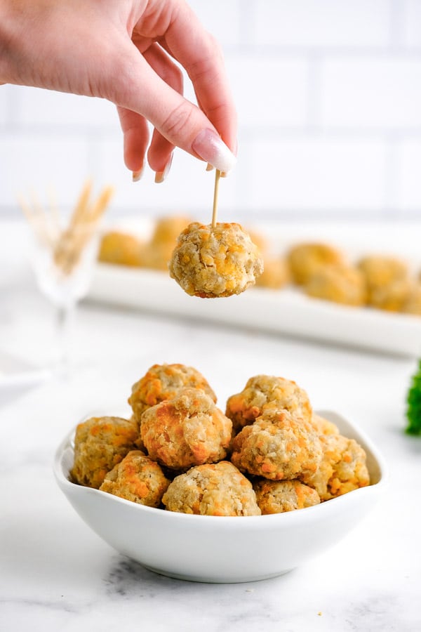 a ladies hand holding a sausage balls by a toothpick over a bowl of sausage balls