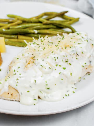 closeup of herb chicken covered with creamy sauce on a plate with potatoes and green beans