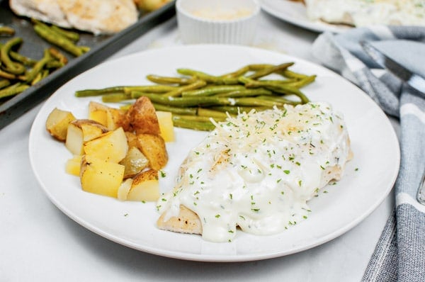 a white plate with creamy sheet pan chicken potatoes and green beans