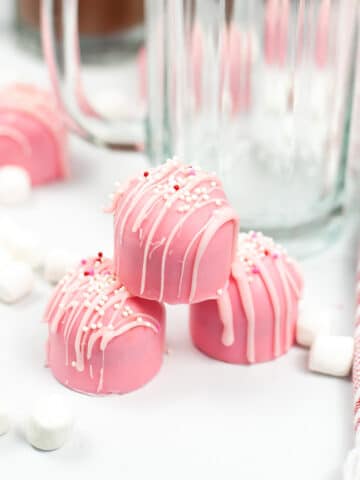 pink hot cocoa bombs with valentines sprinkles stacked on a white table
